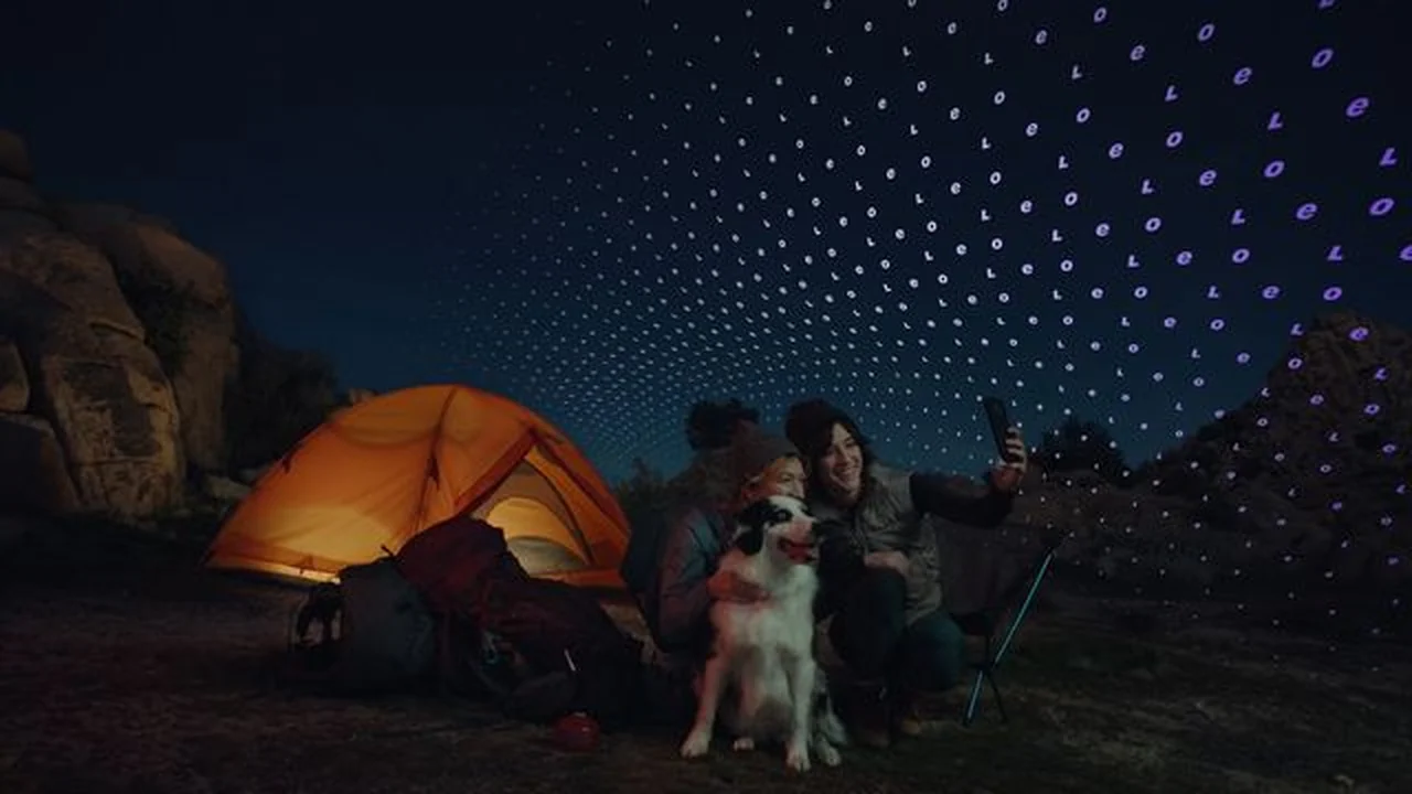 Zwei Menschen mit Hund vor einem Zelt bei Nacht, darüber ein Satellitennetz am Sternenhimmel