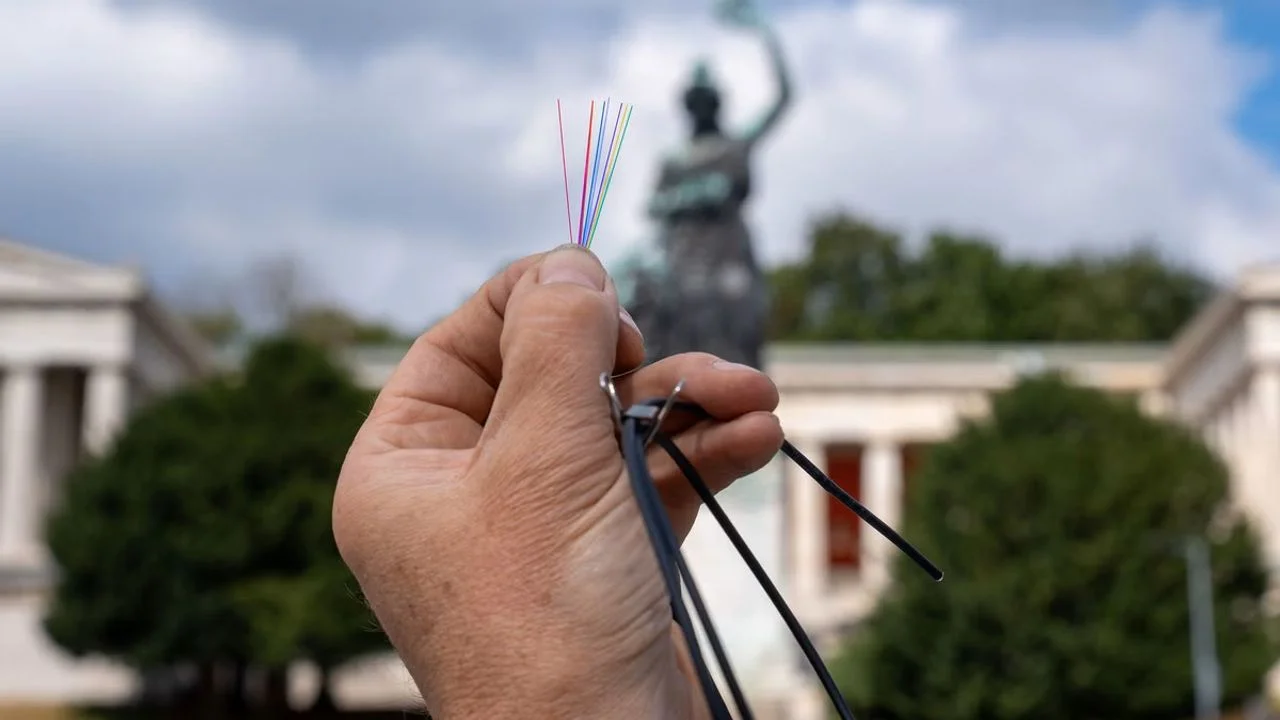 Hand hält Glasfaserkabel vor der Bavaria-Statue auf der Theresienwiese