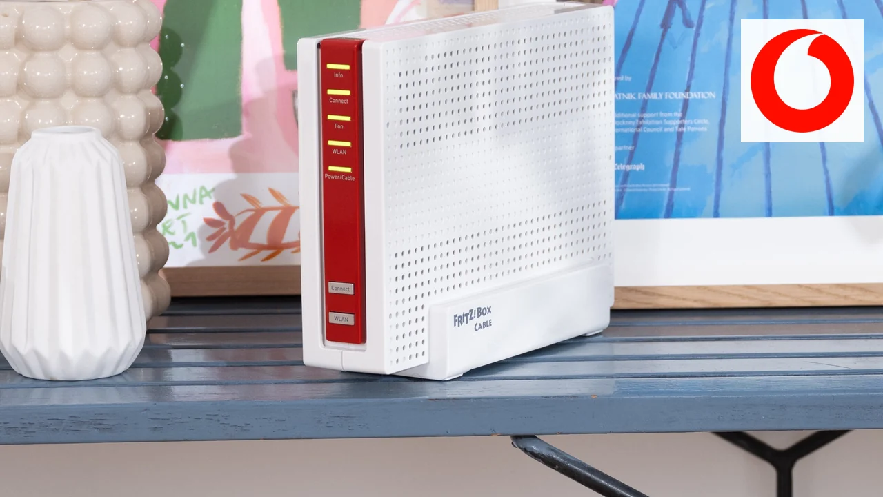 FRITZ!Box 6690 Cable steht auf einem Sideboard vor bunten Bildern, oben rechts das Vodafone-Logo